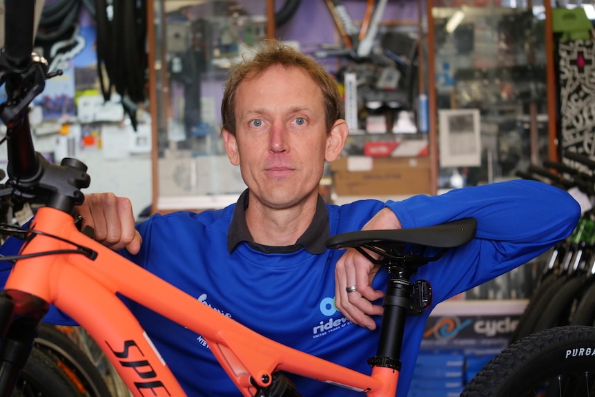 A man in a blue shirt leans on a bike