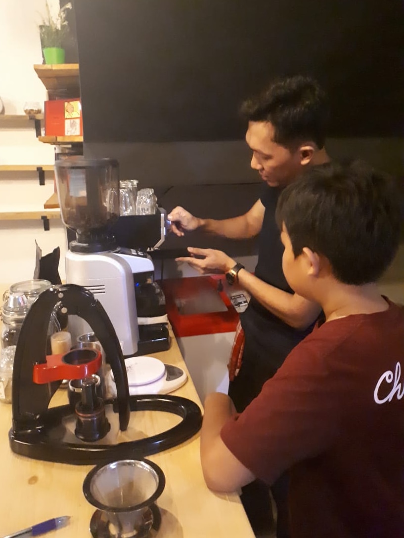 Dany Ismanu works at a coffee machine as another person watches.