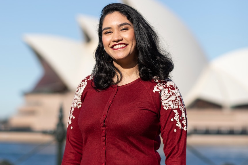 A woman wearing a red dress stands in front of the Opera House.