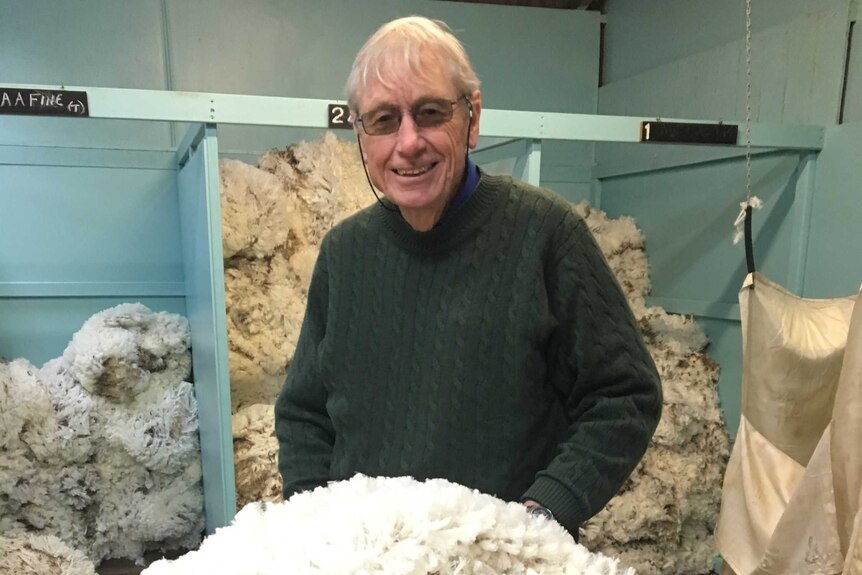 Farmer Simon Cameron stands in a shearing shed, with a pile of wool on the table in front of him.
