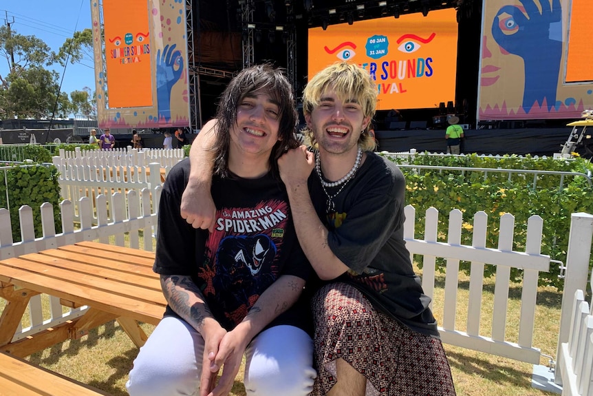 Two men wearing black T-shirts in front of a stage and picket fences