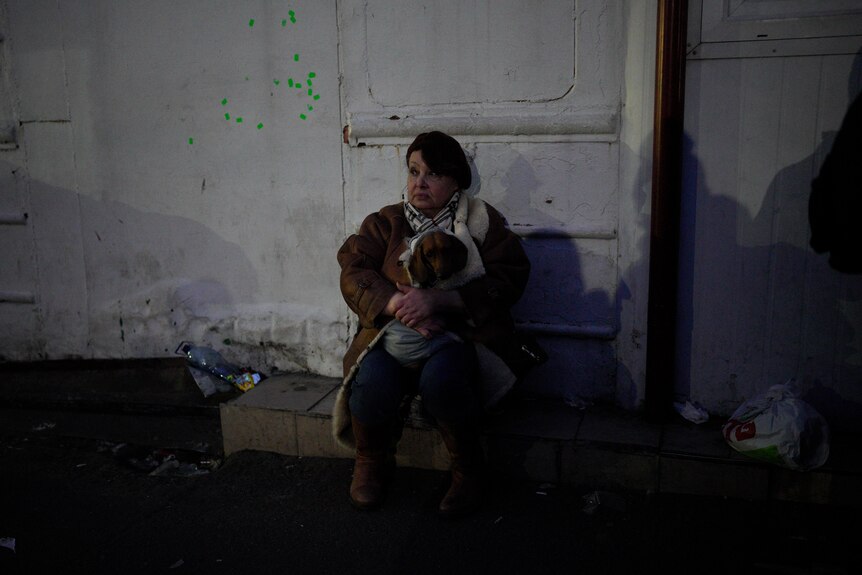 Woman sitting down with her dog on the side of the road against a white wall near the Polish border of Ukraine