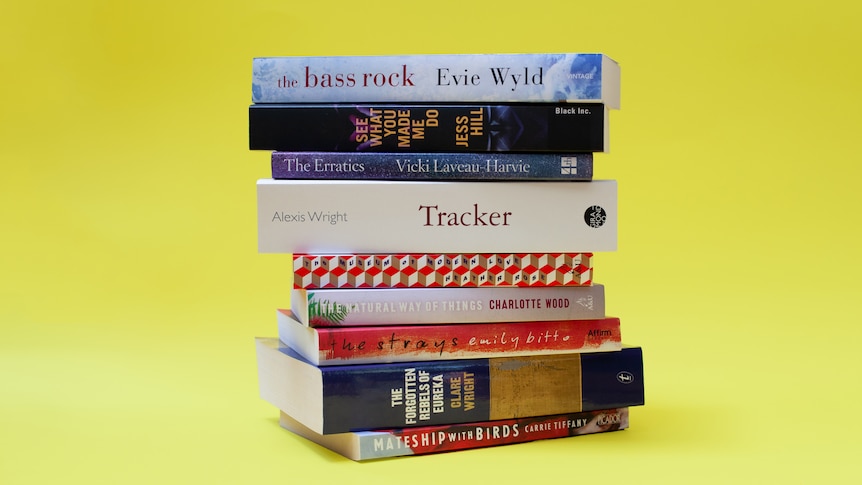 A stack of nine brightly coloured Australian books of different sizes, released between 2012 and 2020, on a yellow background