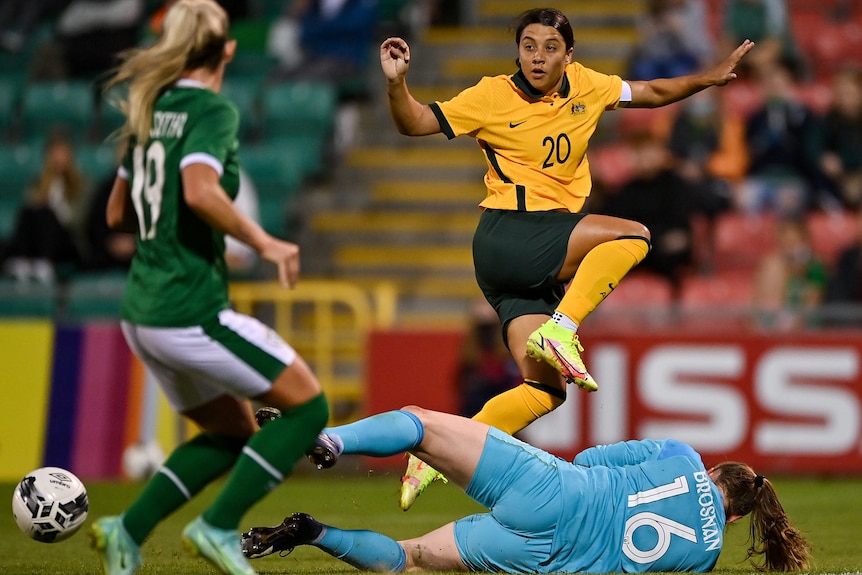 Sam Kerr passes the ball past the goal keeper who is diving at her feet