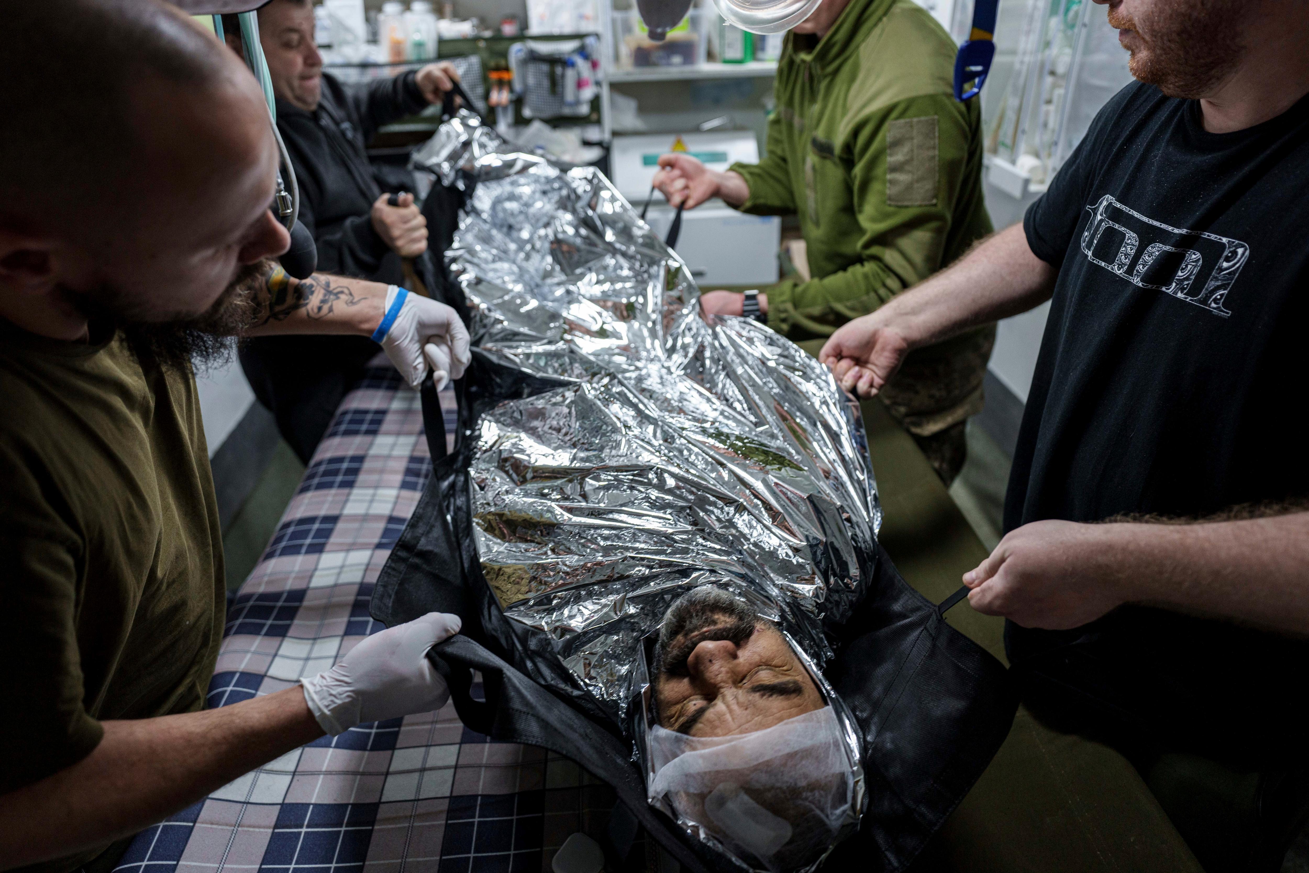 Military medics treat a man wrapped in a thermal blanket.