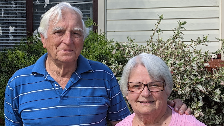 A man and a woman stand in front of a house.