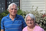 A man and a woman stand in front of a house.