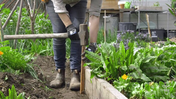 Person hammering a wooden stake alongside a vegetable garden bed edge