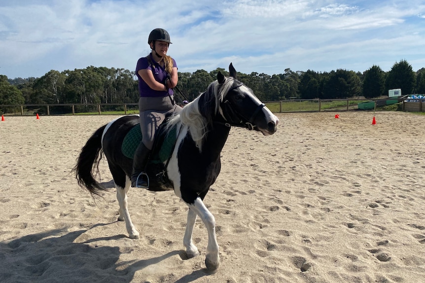 A teenage girl with no forearms rides a horse.