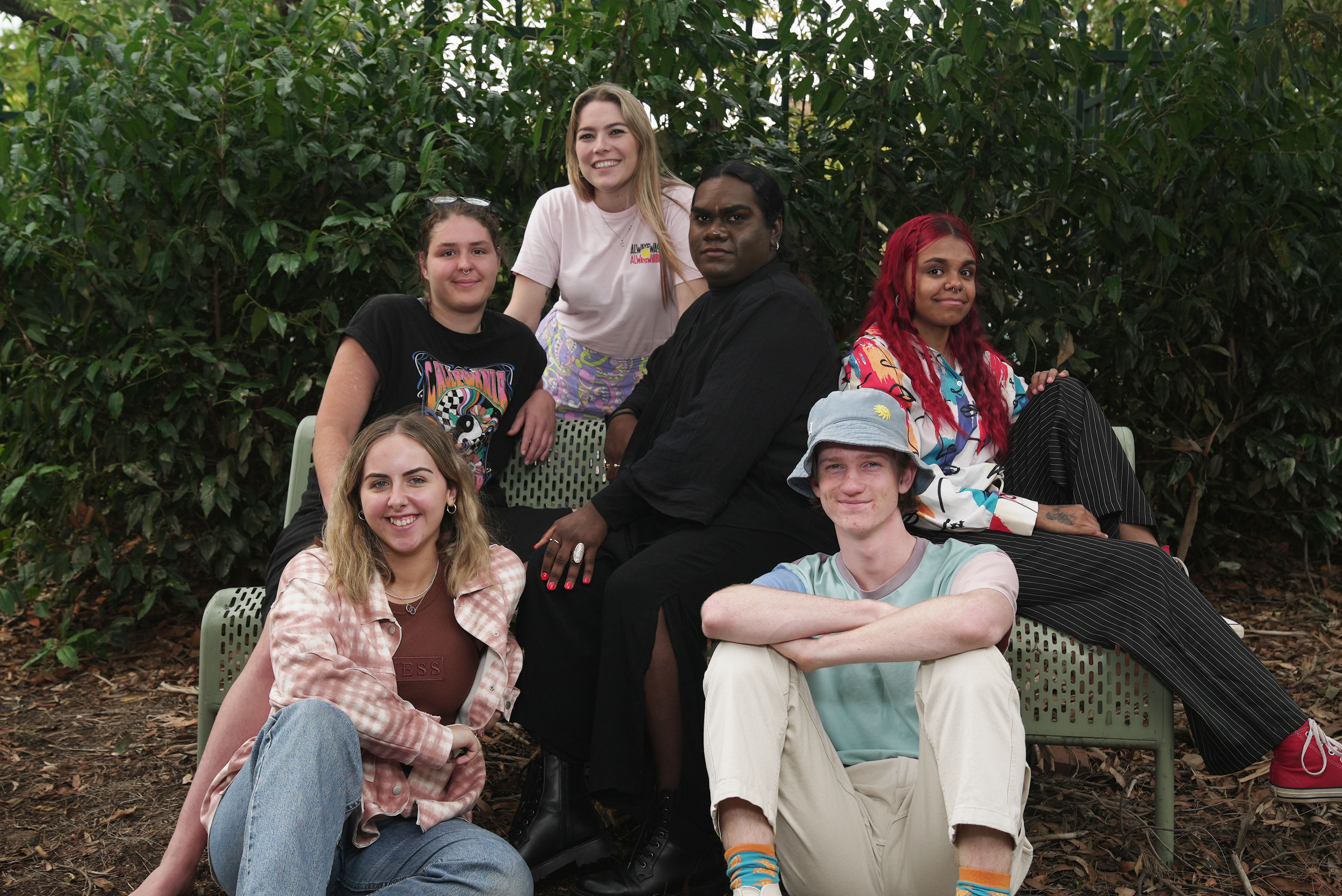 Six people all sit on a couch at different heights, smiling. 