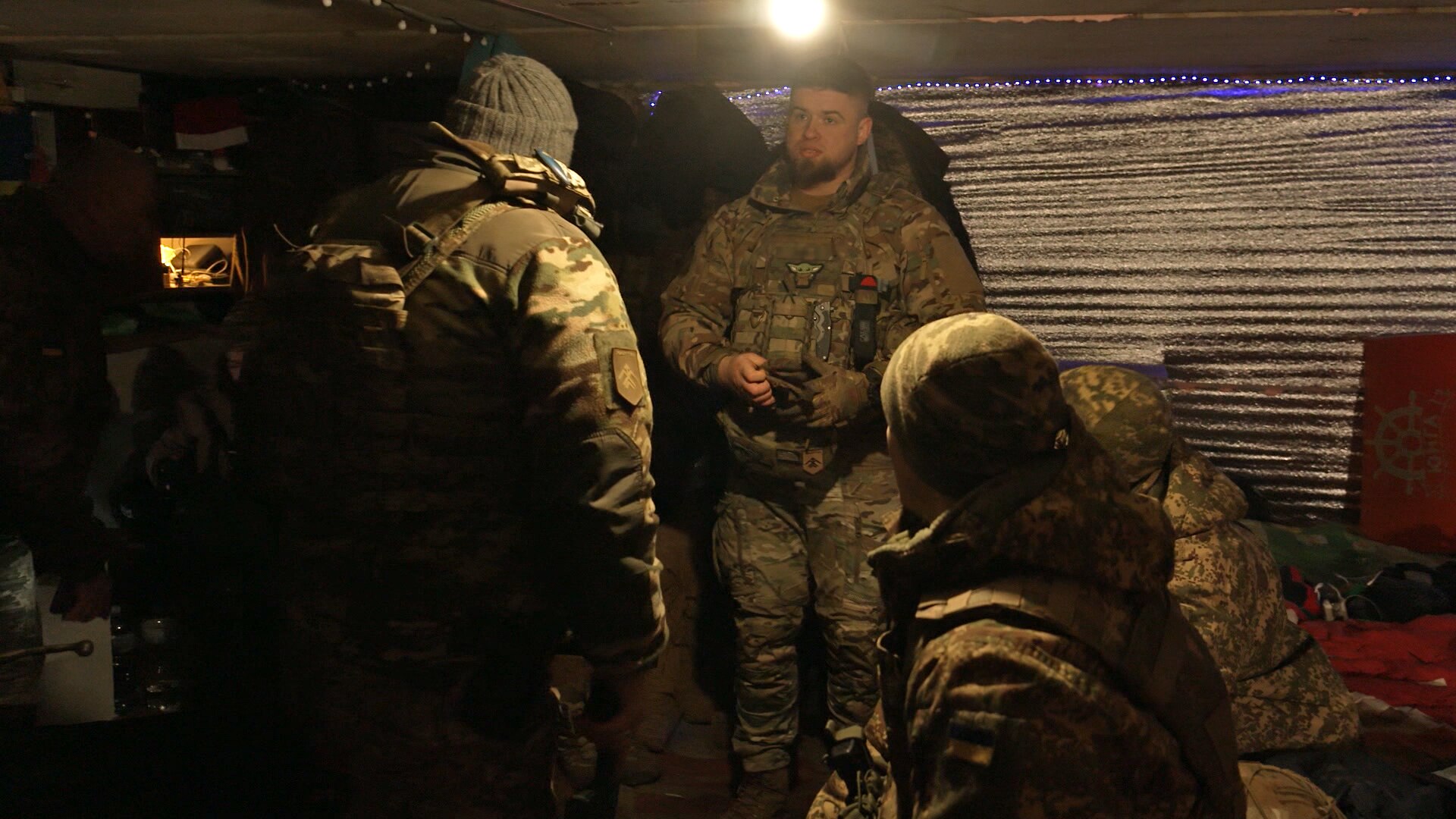 Three men in military fatigues stand in close quarters inside a darkened room.