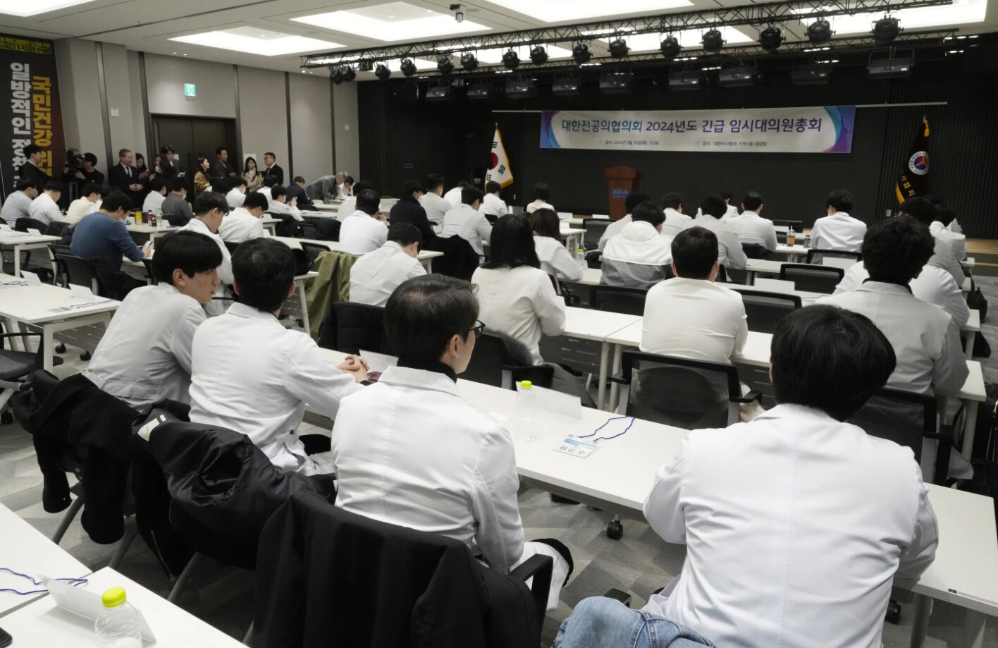 Rows of people sitting down at tables wearing white coats