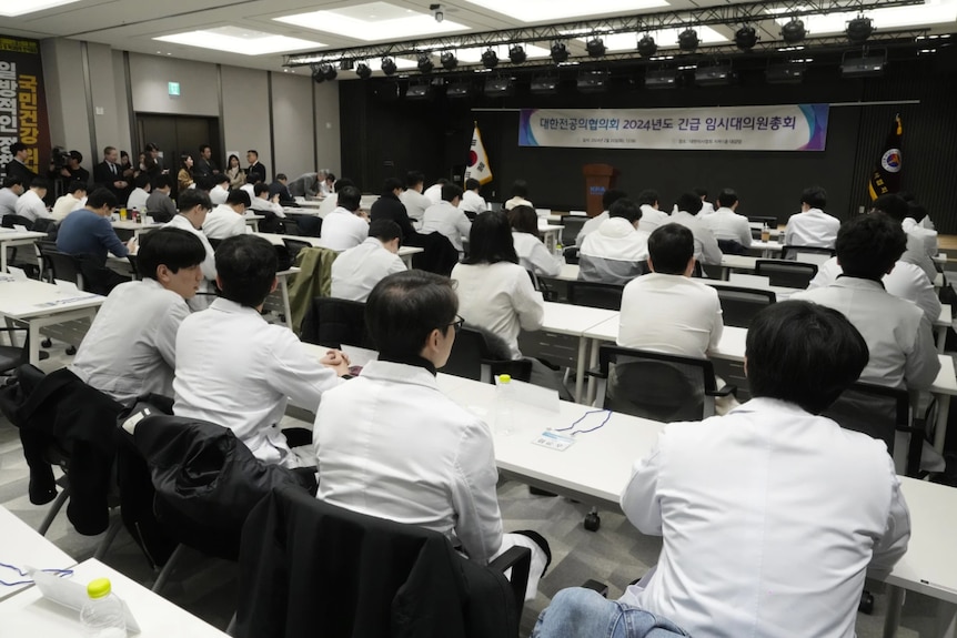 Rows of people sitting down at tables wearing white coats