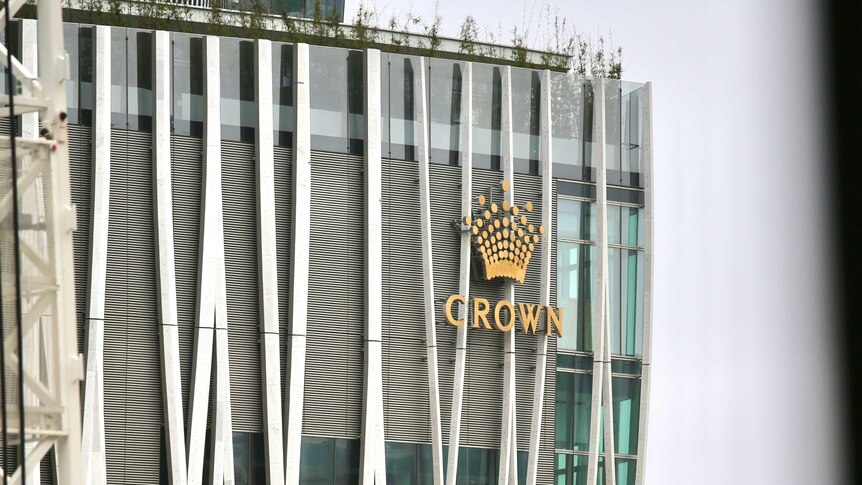 A large multi-storey building made of glass and steel with a gold crown logo on one corner.