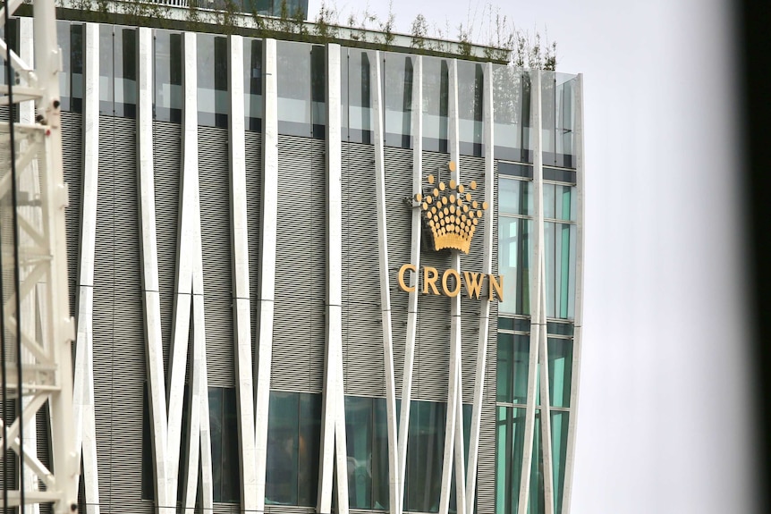 A large multi-storey building made of glass and steel with a gold crown logo on one corner.