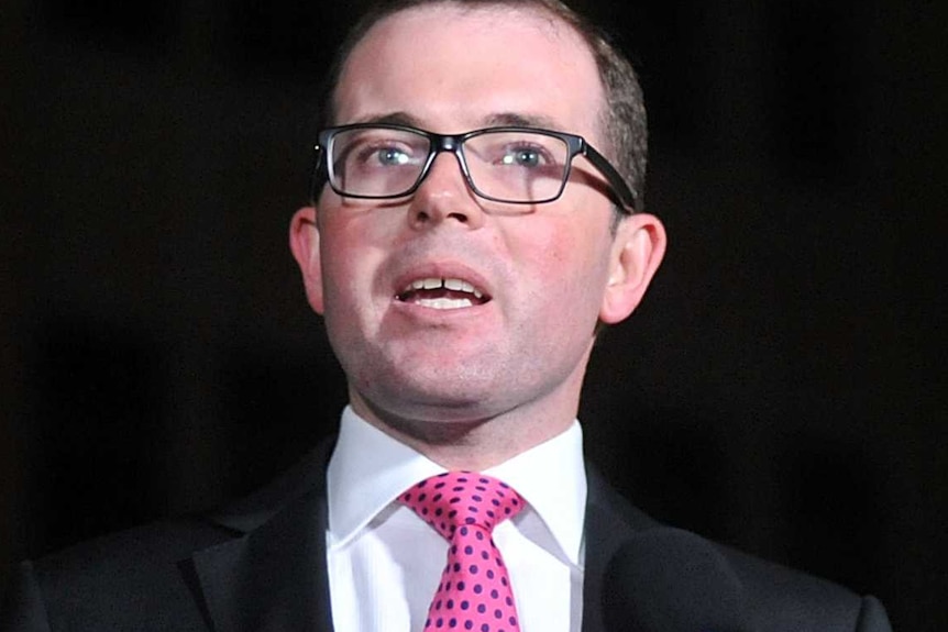 A politician in a dark suit gesticulates as he speaks at a lectern.