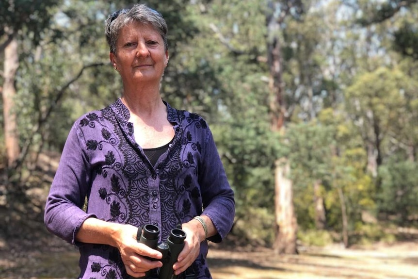 Tasmanian wildlife expert Sally Bryant holding binoculars with the bush behind her.