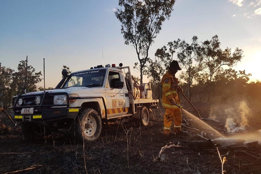 Bushfire NT volunteer with fire unit in background putting out fire.