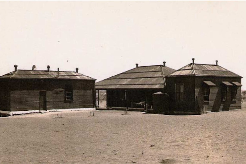 A sepia photo of three buildings which operated as the Port Hedland Lock Hospital surrounded by dirt