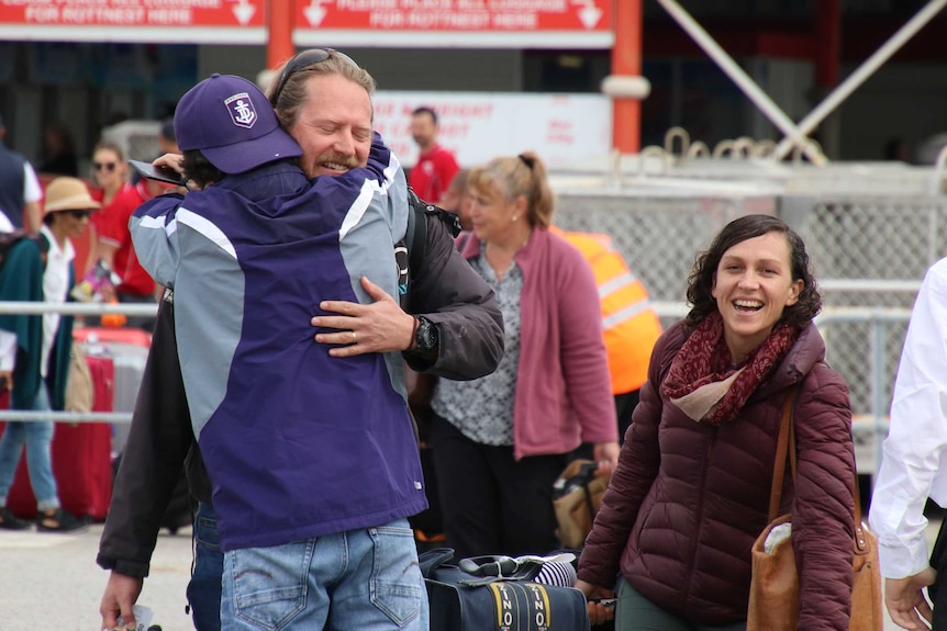 People smile and hug on a ferry wharf.