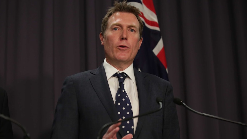 Mr Porter is standing in front of a flag, wearing a navy tie with white dots.