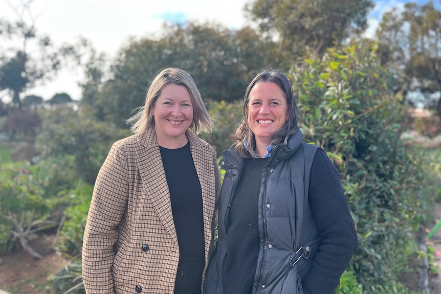 Two women stand outside, smiling.