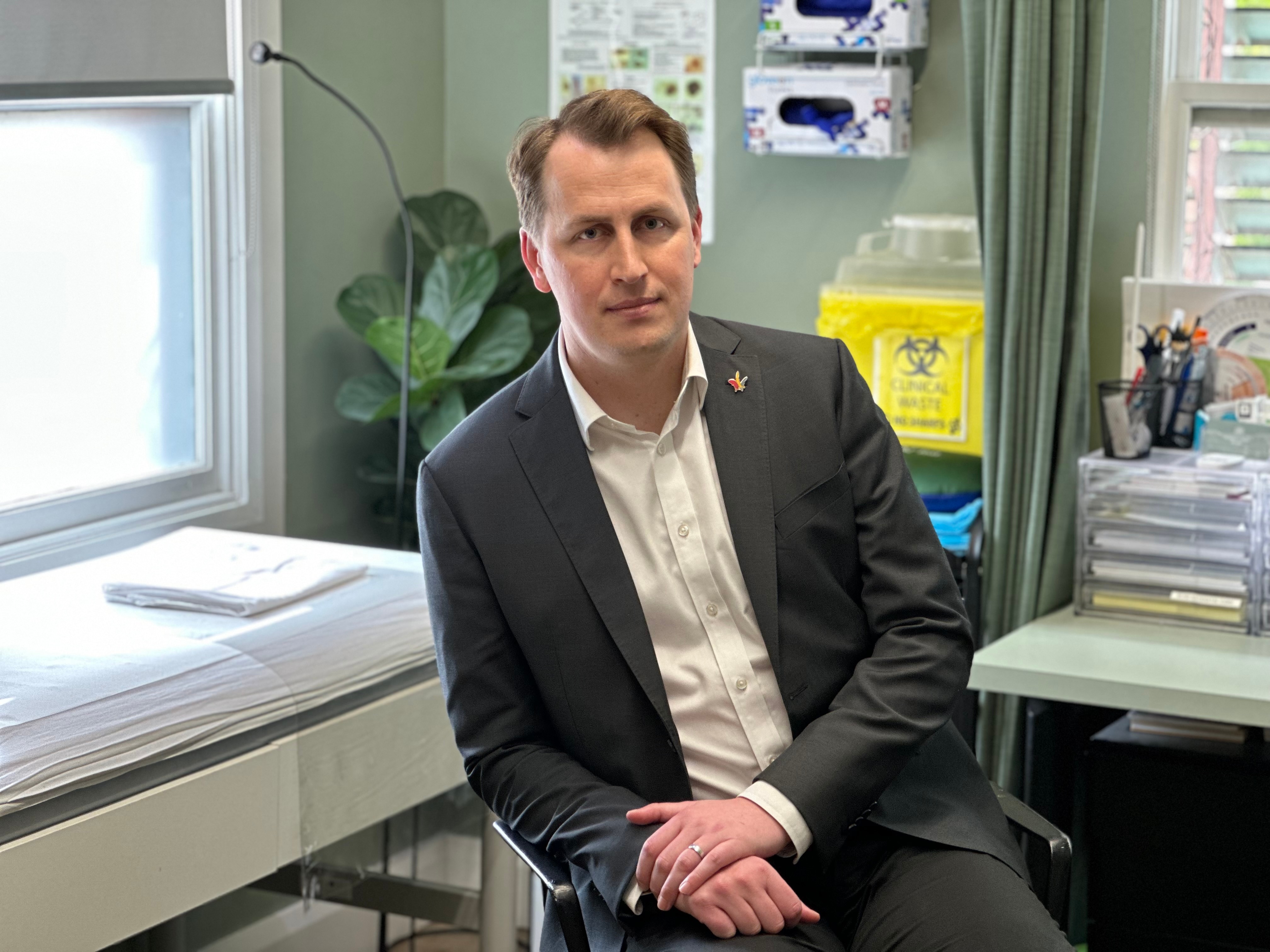 A man wearing a shirt and jacket looks at the camera inside a GP clinic
