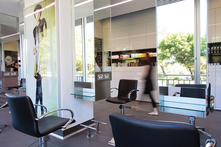 A white hairdressing salon with mirrors, chairs and a person walking past