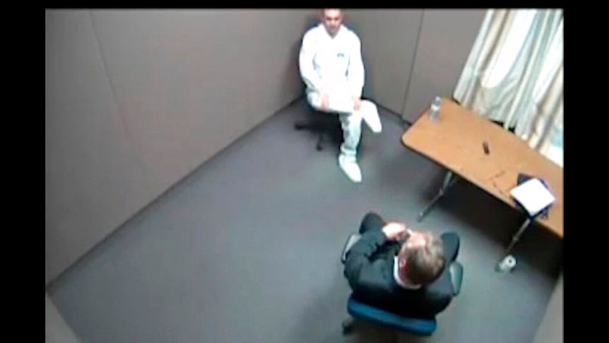 A still from police security camera footage shows two men in a police interrogation room.