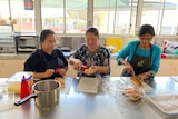 Three women prepare food in a kitchen.