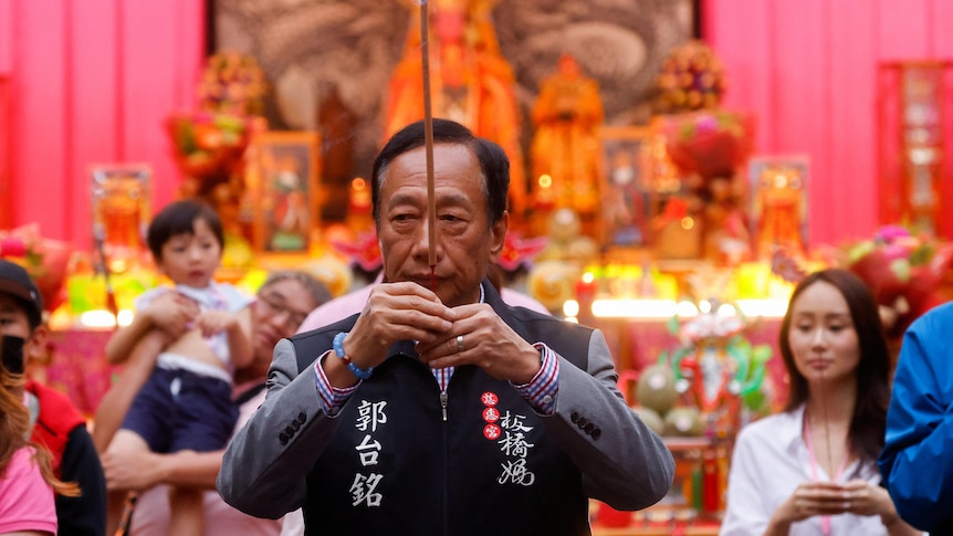A middle-aged man holds a long stick up in a prayer position in front of his face