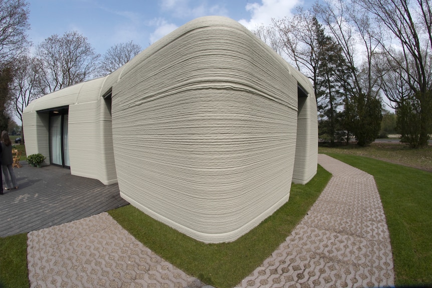 The exterior corner of a 3D printed home shows thin layers of grey concrete stacked to create a wall.