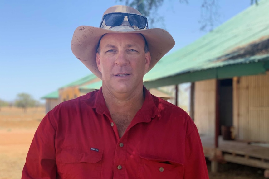 A grazier in a hat poses in front of a wool shed