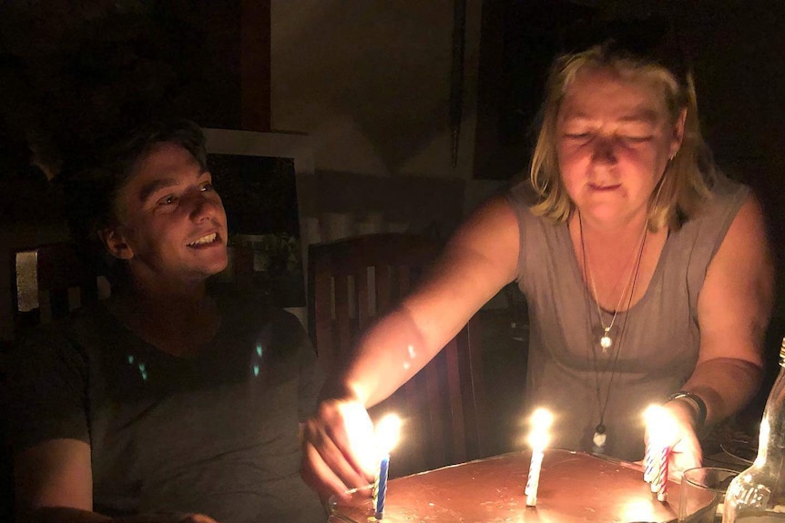 A woman placing a cake on a table with a young man sitting next to her.