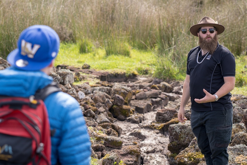 A man explaining, in front of channels used as eel traps.