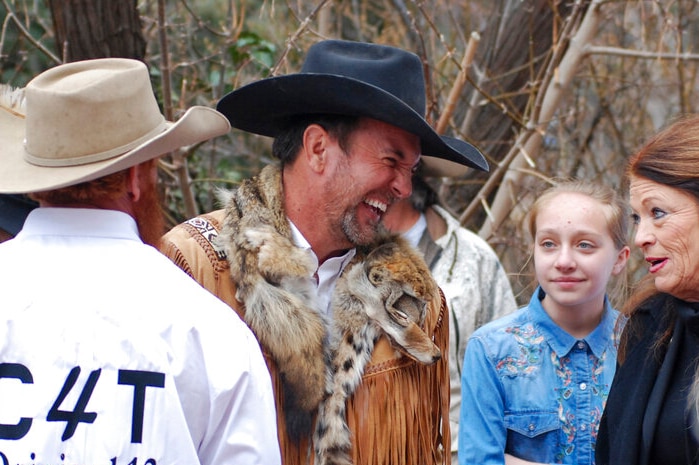 A man laughs while wearing a cowboy had an a fox fur scarf