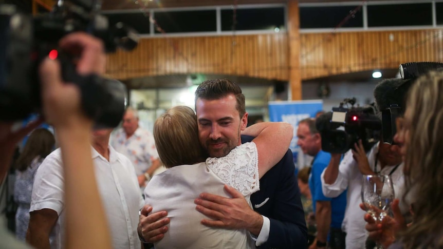 Zak Kirkup hugs a supporter with a half smile with multiple news cameras pointed at him