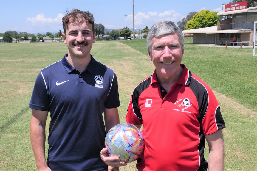 Two men standing on a soccer field, one with a ball in his right hand 