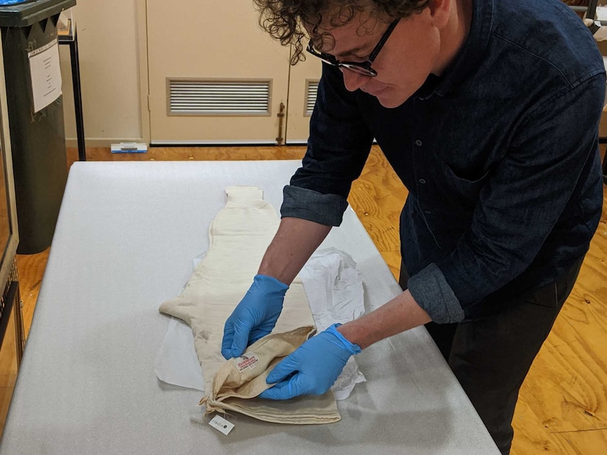 Man carefully showing the label of a pair old woollen long johns lying flat on a table