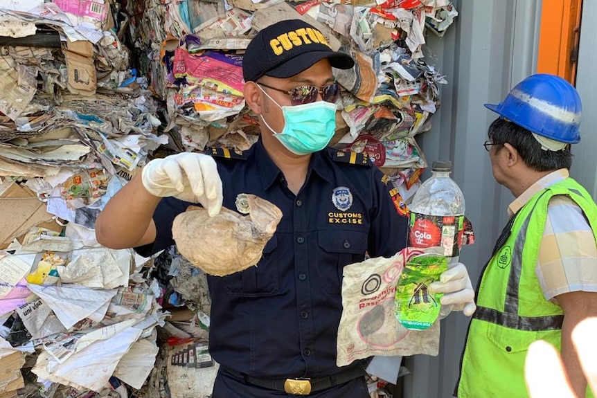 An Indonesian customs official holds up a dirty nappy in front of a shipping container full of paper.