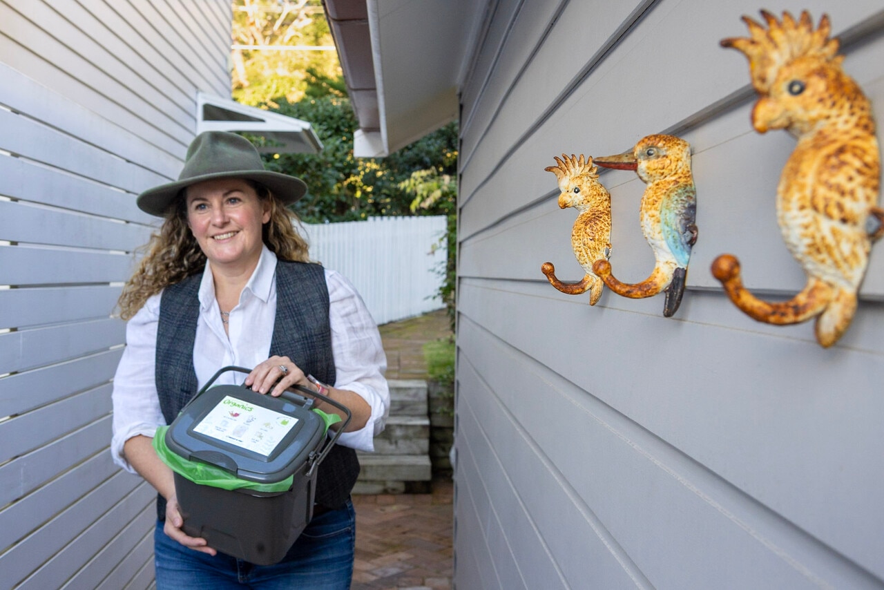 A woman holds a compost bin.