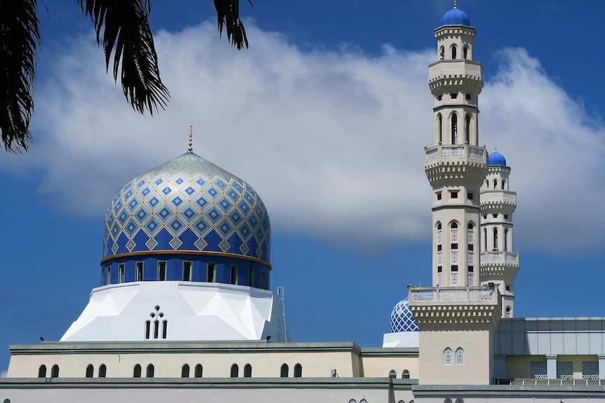 Minarets and the dome of a mosque in front of blue sky in Malaysia.