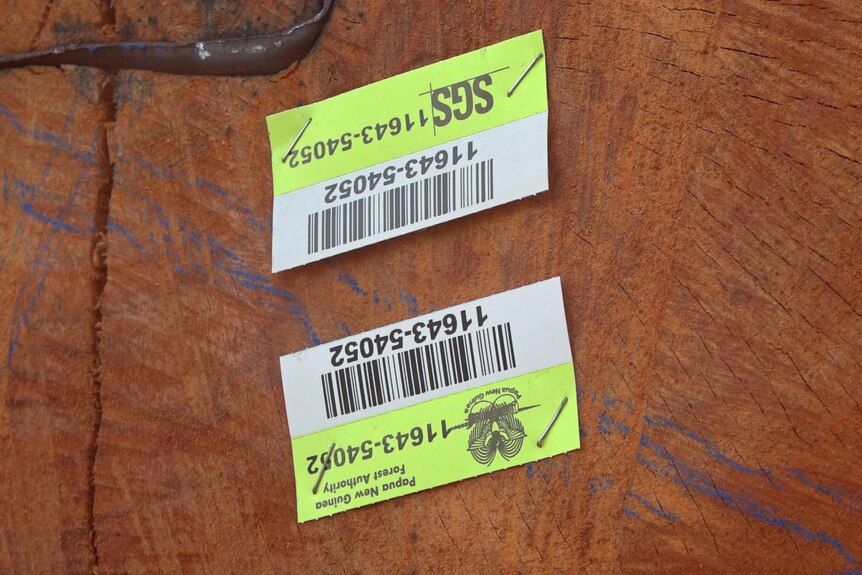 Two paper barcodes stapled to the end of a log. Words on the paper say "Papua New Guinea Forest Authority".