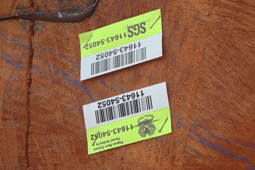 Two paper barcodes stapled to the end of a log. Words on the paper say "Papua New Guinea Forest Authority".