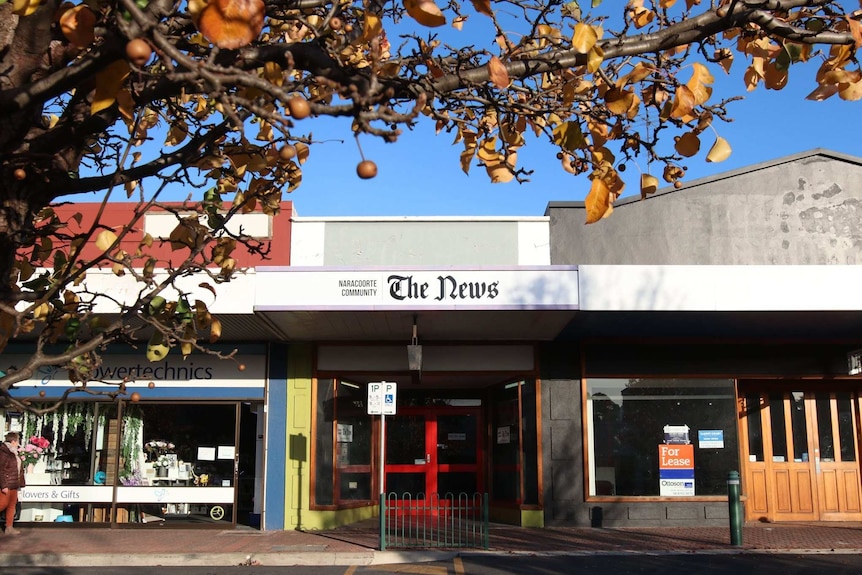 A small shop front with green wall, red doors and a sign reading  'Naracoorte Community - The News' sits between two shops.