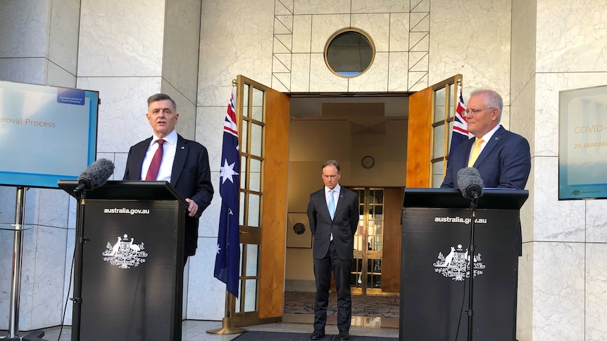 Three men stand in a courtyard with two lecterns