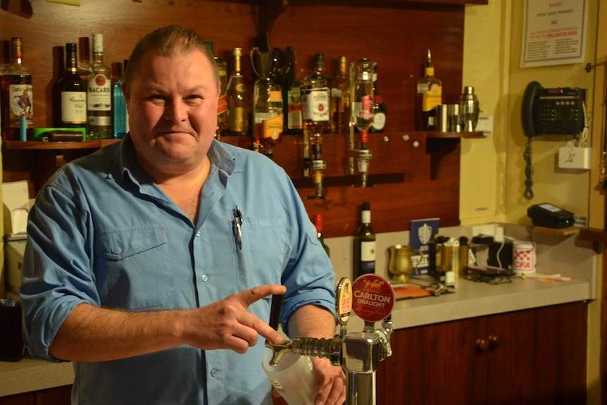 A man stands behind the beer tap with a glass ready to go.