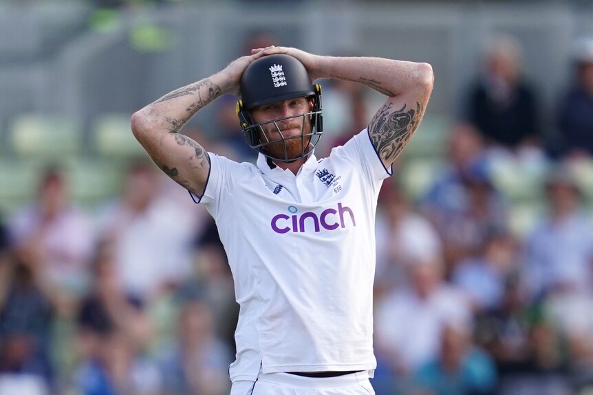 Ben Stokes holds his head while wearing a helmet
