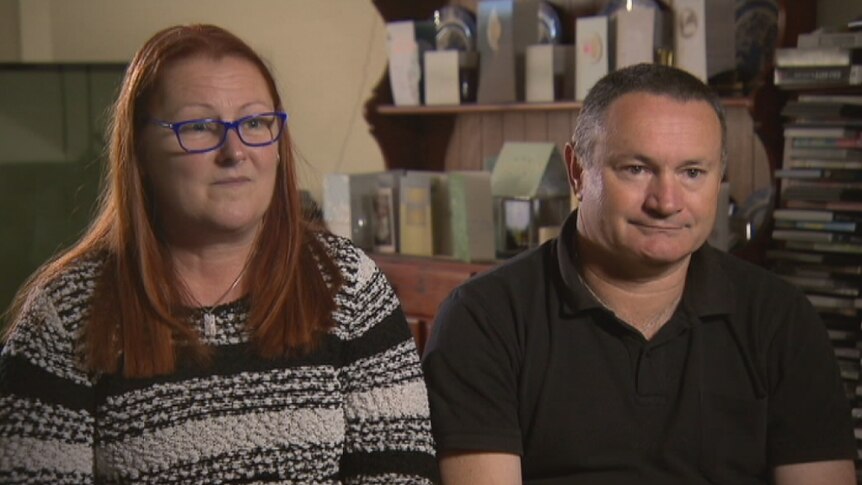 The mother and step father of Jason Challis sit in a lounge room looking at a camera with sad expressions.