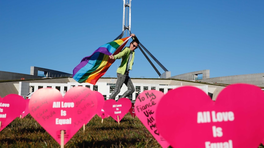 Protester carries rainbow flag in front of Parliament House